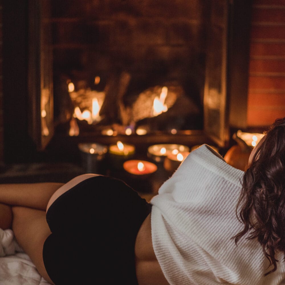 Woman lying in front of a fireplace is wearing a white sweater and black high waist underwear.