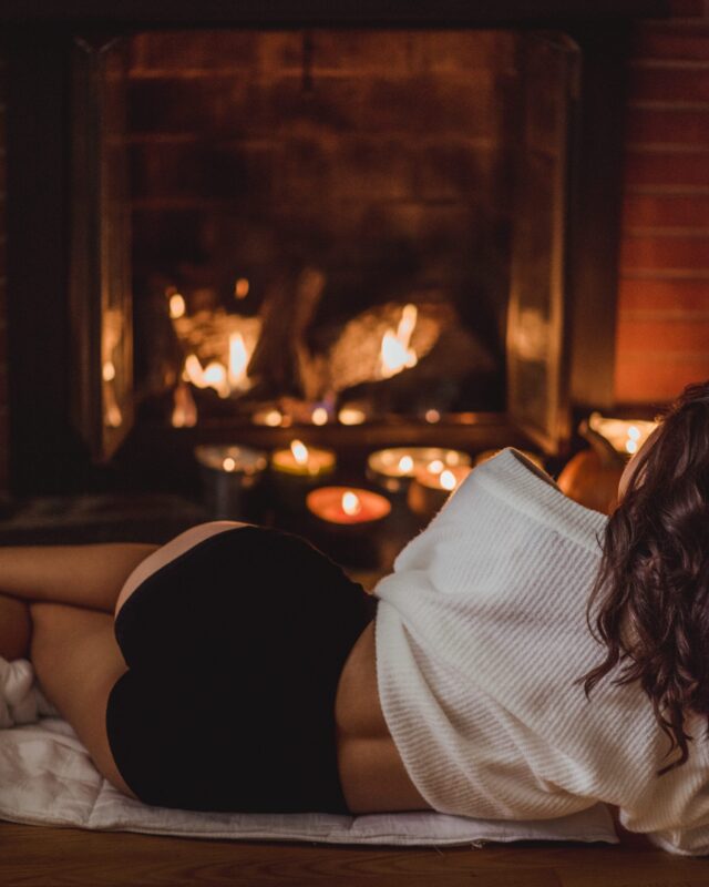 Woman lying in front of a fireplace is wearing a white sweater and black high waist underwear.