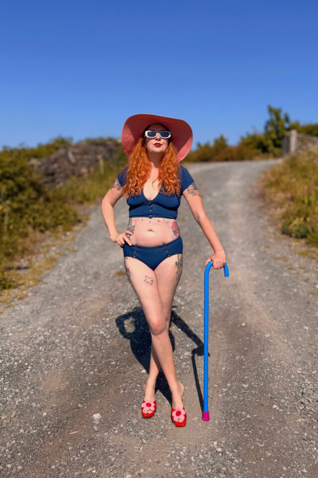 Model wearing the Magnet Inge adaptive magnetic crop top in deep blue, featuring a low-V neckline and front magnetic closure, standing outdoors on a sunny road.